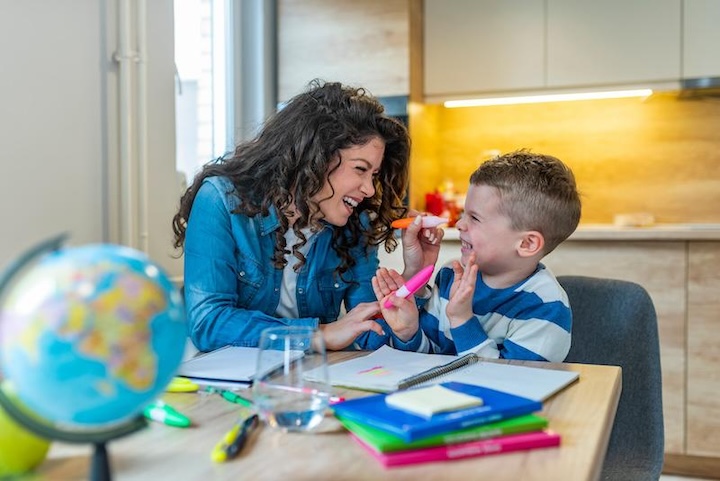 Mother helping with homework to her son indoor. Family, children and happy people concept. Mother and sons drawing together, mom helping with homework