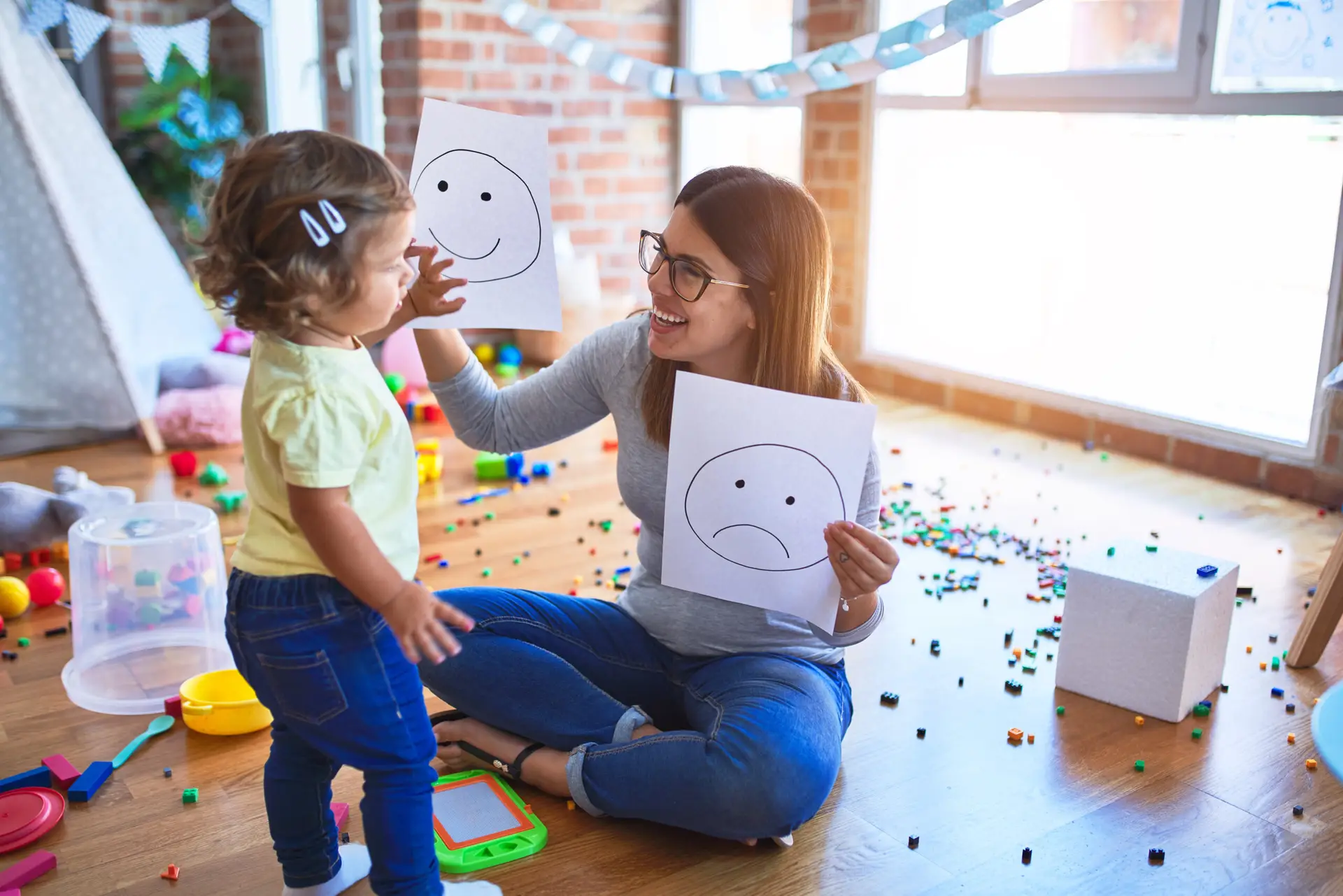 Teacher working with child, holding happy face drawings
