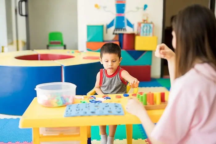 Child playing with letter toys at play table while being supervised