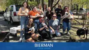 A group of Bierman Autism Centers team members smiles for a photo outdoors, holding small animals like bunnies and goats. They are surrounded by petting zoo enclosures and trees, reflecting a fun, team-centered atmosphere.