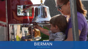 Mother supports toddler ringing a quiet fire-engine bell at Bierman Autism Centers’ sensory-friendly Touch-a-Truck event.