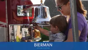 Mother supports toddler ringing a quiet fire-engine bell at Bierman Autism Centers’ sensory-friendly Touch-a-Truck event.