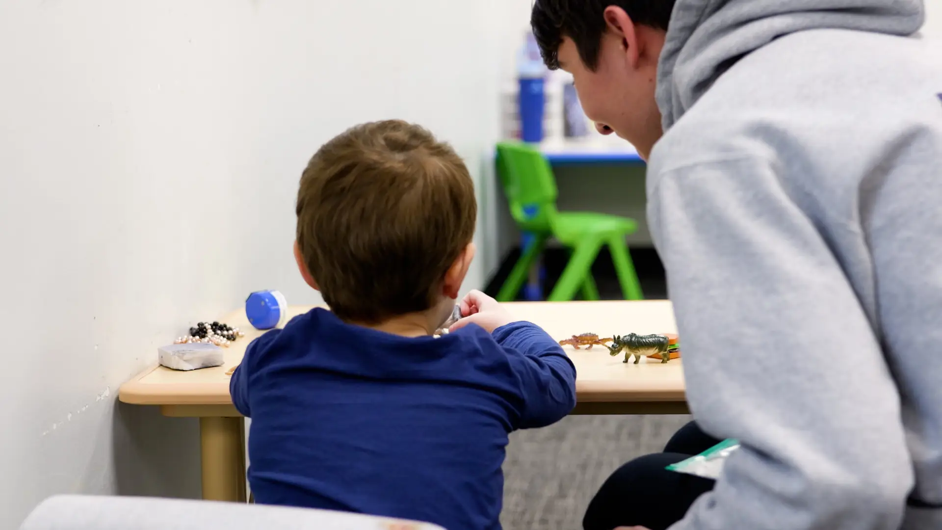 BCBA clinician supports a young child playing with toy dinosaurs during an ABA therapy session at Bierman Autism Centers.