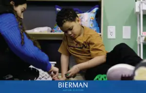 An adult and a young boy sorting small toys from a basket on a therapy room floor.